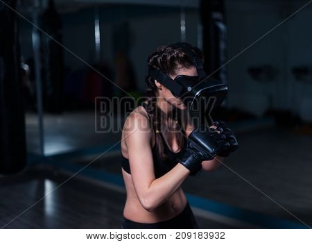 Young fighter boxer fit girl in VR glasses wearing boxing gloves in training defending from unseen enemy. Boxing game in virtual reality 360 degrees. Futuristic gaming