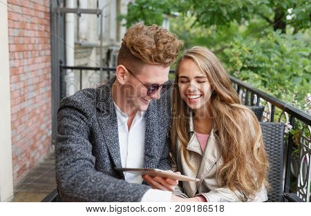Cheerful attractive young boyfriend and girlfriend holding a digital wireless tablet and relaxing at the cafe on a blurred background.