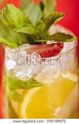 Summer Drink - White Sparkling Sangria. Sangria Drink with Orange, Strawberry and Mint on Bright Red Background. Leaves and Flower on Background