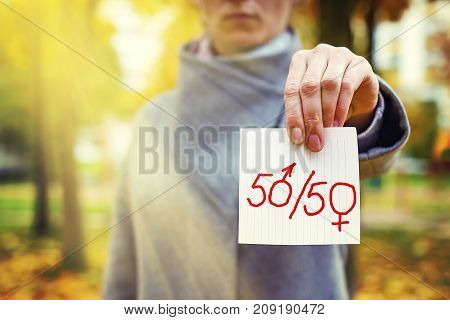 gender parity concept. close up young caucasian woman holding in hand paper with written text 50/50 with zeros as male and female gender symbols. Human rights day