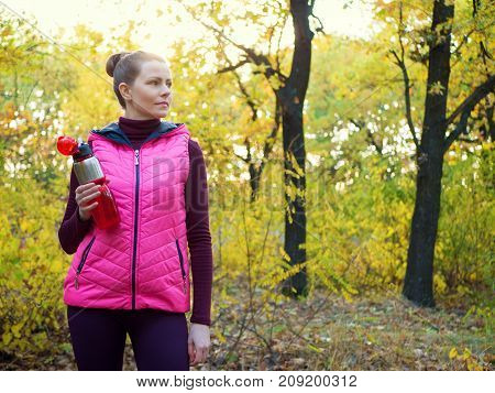 Beautiful fitness sport girl in sportswear with sports water bottle or isotonic drink in hand in autumn forest