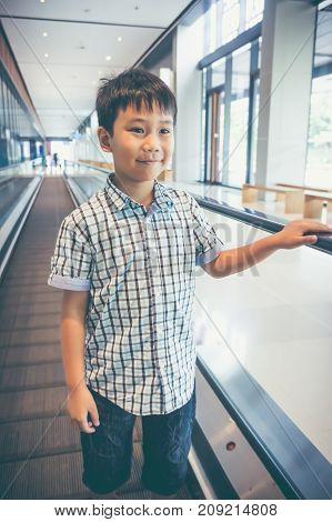 Happy Asian Child Standing And Smiling On Electric Speedwalk At Modern Airport.