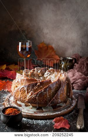 Bundt cake with saffron and rum covered with white glaze on rustic background with autumn decorations