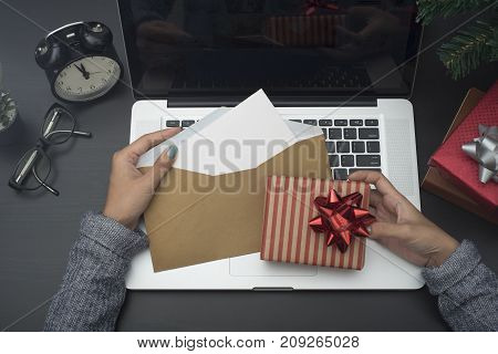 business woman hand holding christmas card and gift box on desk. concept office christmas and happy new year.