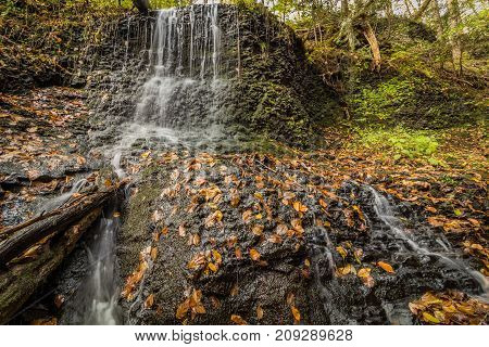 Waterfalls flow smoothly over rocks surrounded by fall foliage in Deleware Water Gap section of Pocono Mountains, PA