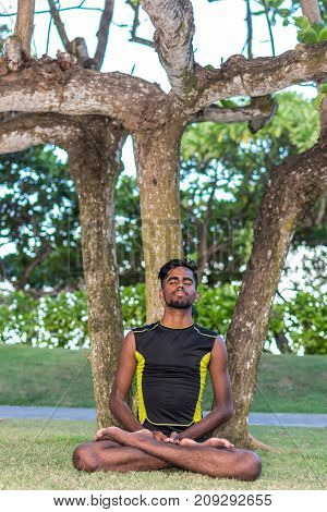 Young yoga man practitioners doing yoga on nature. Asian indian yogis man on the grass in the park.