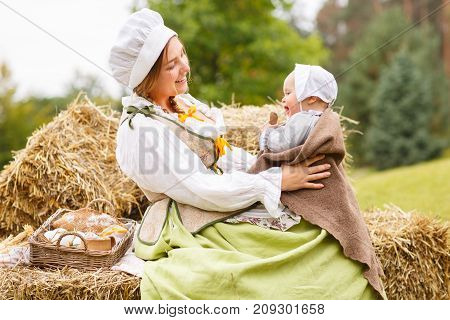 Happy peasant mother with little baby in summer playing on haystack in the field