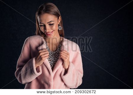 Portrait of a young beautiful girl in stylish necklace and earrings decorations on a dark background