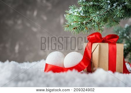 Christmas gift box with red ribbon and balls on snow on grey background. Christmas or New Year background with fir branches decorations and gift boxes with copy space. Christmas surprises.