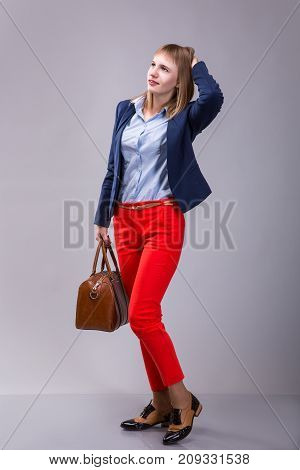 girl in red pants with a leather bag looking into the distance over gray background