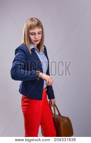 girl in red pants and with leather bag looking at watch over gray background