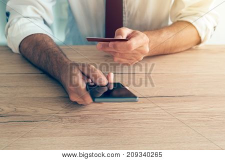 Mobile banking smartphone app used by businessman at office desk. Adult caucasian business person connecting credit card to online internet e-banking service.