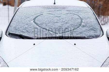 Heart love symbol on windscreen of car in snow. Front view of snowy car after winter blizzard
