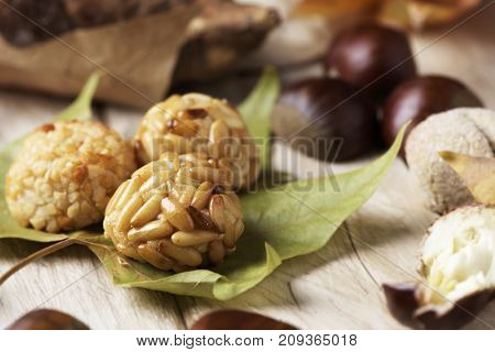 closeup of some chestnuts, some panellets and a roasted sweet potato, as a typical snack eaten in All Saints Day in Catalonia, Spain, called castanada, and some autumn leaves on a wooden table