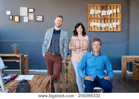 Portrait of three casually dressed work colleagues smiling confidently together while working in a large modern office