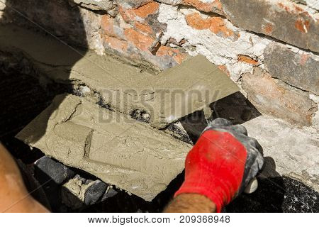 Worker with wall plastering tools renovating house. Plasterer renovating outdoor foundation and walls.