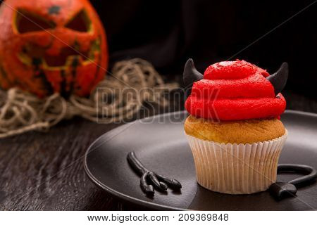 Halloween red one cupcake in the shape of the devil. Cupcake with horns and tail. Halloween decorated cookie on dark wooden table. Close up