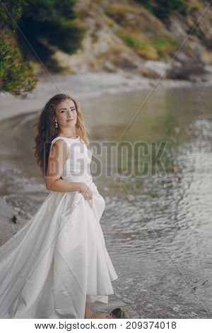Beautiful long-haired bride in a magnificent white dress walking on a beach