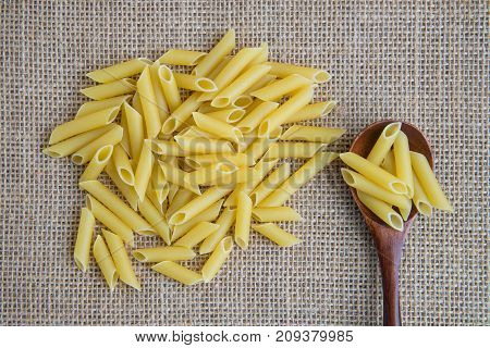 Penne raw pasta in wooden spoon on sack rustic background . Natural and healthy food concept