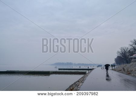 BELGRADE SERBIA - JANUARY 18 2015: People walking with umbrellas near the Danube river during a heavily foggy and rainy winter afternoon in Zemun a northern district of Belgrade