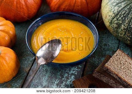 Bowl of healthy vegan pumpin soup with sesame seeds served with rye bread and organic pumpkins closeup