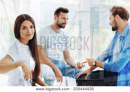 Pleased with day. Young positive woman sitting on the chair while her friends having discussion and expressing interest