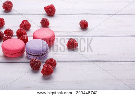 Delicious colorful biscuits macaroons with raspberries over white wooden background. Place or space for text