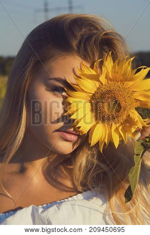 close-up portrait of a european blonde girl with blue eyes holding a sunflower in her hand that covers the face