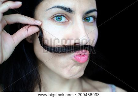 Portrait of a young beautiful woman with dark hair holding a strand of her hair over her upper lip. The concept of the problem of removing excess hair on the face of women.