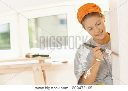 Woman renewing home. Happy young woman painting wall with paint brush in her fixer upper, smiling.