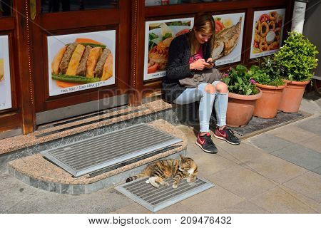 Istanbul Turkey - April 22 2017. Street scene in Istanbul with girl sitting and holding a smartphone and cat lying in front of kebab shop in Istanbul.
