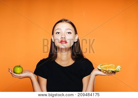 a sad girl chooses that it is better to eat an apple or a mouth-watering sandwich. A girl wants to bite an apple, healthy food, delicious food