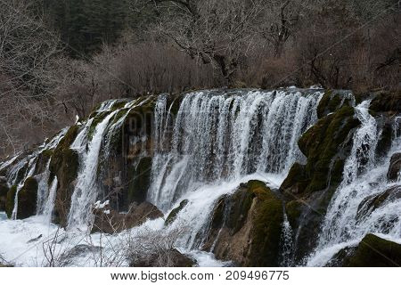 Waterfall in the forest. Frozen water drains over the rocks. The rock is covered with moss on which cold water flows.Water flow to rocks