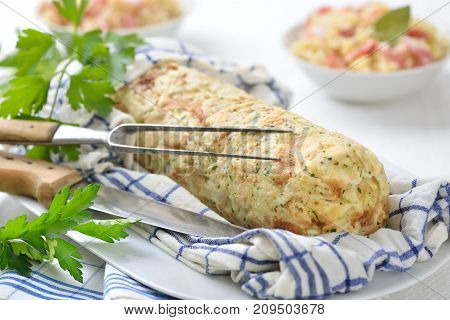 Uncut Bavarian bread dumpling cooked in a rolled up tea towel, sauerkraut with bacon in the background