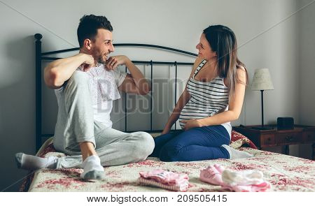 Young man showing baby clothes to her pregnant wife