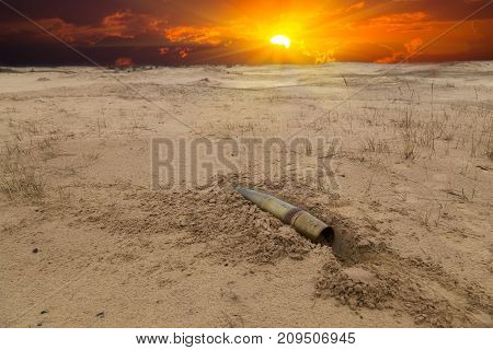 old artillery metal projectile on the sand in the desert against the background of a blood-red dramatic sunset. concept of war