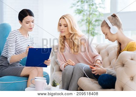 Daughters diagnosis. Serious nice blonde woman sin the psychologists office and looking at doctors notes while worrying about her daughter