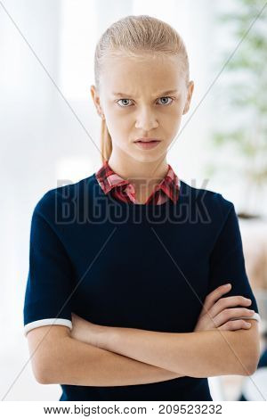 Angry look. Cheerless nice blonde girl standing cross handed and looking at you while being angry