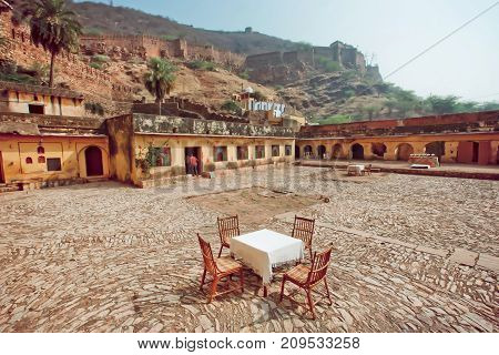 Weird restaurant outdoor on ancient indian house courtyard. Empty table with tablecloth and chairs whithout people and with natural background of Rajasthan, India.