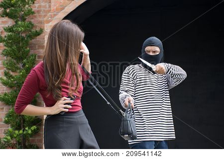 Male robber robbing a handbag threatening with knife to scared Asian woman,criminal concept