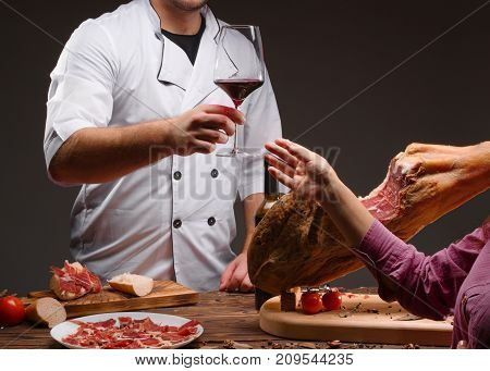 Spanish jamon on a wooden stand, white young girl taste wine with chief, chopped jamon, tomatoes. whine glass and red wine Horizontal photo