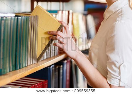 A woman's hand chooses a book in the library. Close-up . The concept of education.