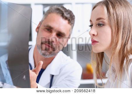 Mature male doctor hold in arm and look at xray photography discussing it with female patient portrait. Bone disease exam medic assistance cancer test healthy lifestyle hospital practice concept