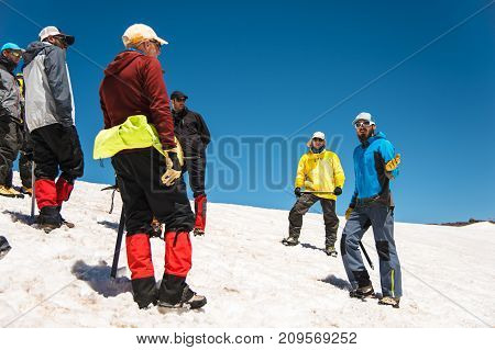 Training to correct slip on a slope or a glacier with the help of an ice ax. A young guide with a beard explains to his group how to properly slow the slip on the slope with the help of an ice ax. Preparation before climbing to the top of the mountain
