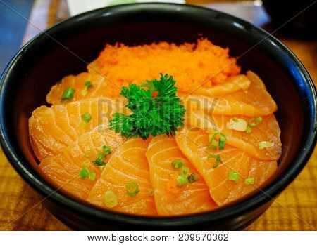 Close up salmon sashimi and  ebiko with rice in black bowl