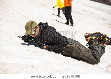 Training to correct slip on a slope or a glacier with the help of an ice ax. A fully equipped backpacker slides on the belly along a snowy slope in the mountains, hindering the glide by an ice ax. Training an inexperienced climber before climbing a mounta