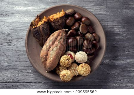 high-angle shot of an earthenware bowl with some chestnuts, some panellets and a roasted sweet potato, as a typical snack eaten in All Saints Day in Catalonia, Spain, called castanada, on a table
