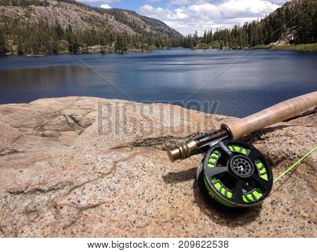 An Angler rests a flyrod upon a granite boulder next to a calm, serene, high elevation, alpine lake .