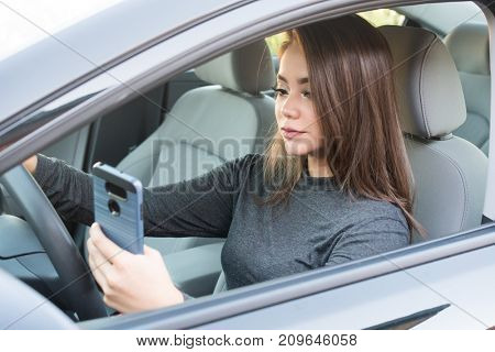 Happy teen girl driving a new car while texting