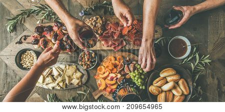 Flat-lay of friends hands eating and drinking together. Top view of people having party, gathering, celebrating together at wooden rustic table set with different wine snacks and fingerfoods